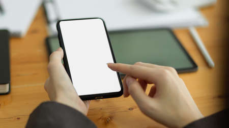 Close-up Smartphone white screen for montage your graphic and touched by female hands. workspace in the backgroundの写真素材