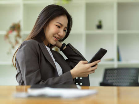 A pleased millennial female employee relaxed on her smartphone, scrolling through social media, watching videos, and shopping online.の写真素材
