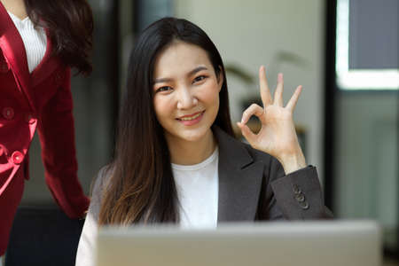 Attractive millennial businesswoman showing ok hand sign to camera, agreement gesture, doing fine, approve, happy.の写真素材