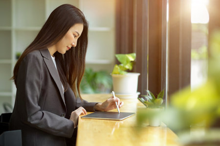 Side view of Attractive asian businesswoman in casual suit sits in a modern bright cafe working on portable tablet computer.の写真素材