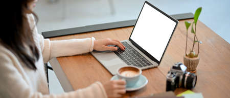 Close-up of a female freelance photographer or cafe blogger selecting a photograph, working, and writing a cafe review on her laptop computer at a cafe.の写真素材