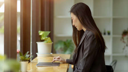 Side view of a female freelancer in casual suit checking her banking account, working on her portable tablet in coffee shopの写真素材