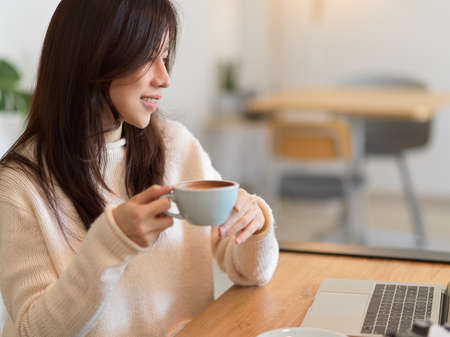 Young beautiful woman drinking morning coffee while working on laptop computer at cafe bar.の写真素材