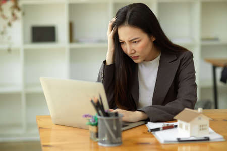 Pensive, Thoughtful, Serious, Ponder young asian businesswoman working on her laptop computer in office.の写真素材