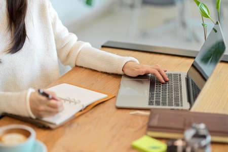 Side view of an attractive female business owner using a laptop to analyze and plan her business model and a notebook to jot down ideas.の写真素材