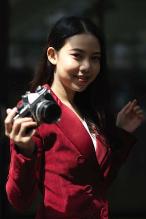 Portrait of Attractive young female photographer in red suit holding retro or vintage camera.の写真素材