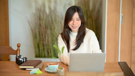 Young asian female photographer or travel blogger working on laptop computer at minimalist Japanese style coffee shopの写真素材