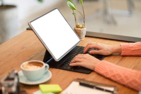 Cropped image of young female freelance travel blogger typing on keyboard, using digital tablet to update her online content.の写真素材