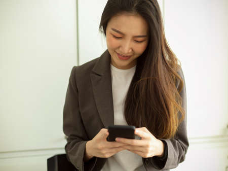 Professional asian businesswoman sits in office using smartphone to read information, social media application, chat with her friendsの写真素材