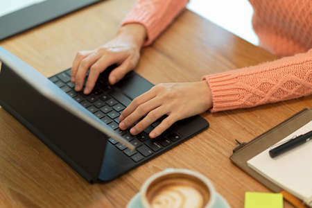 Cropped image of Female in pink sweater typing on keyboard, working on portable tablet computer at cafe desk.の写真素材