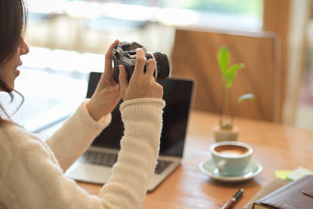 Beautiful asian female holding vintage camera, sitting at portable workspace in cafe.の写真素材