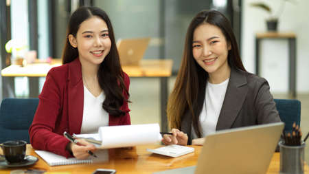 Happy and friendly attractive Asian businesswomen or accountants collaborate at their office desk.の写真素材