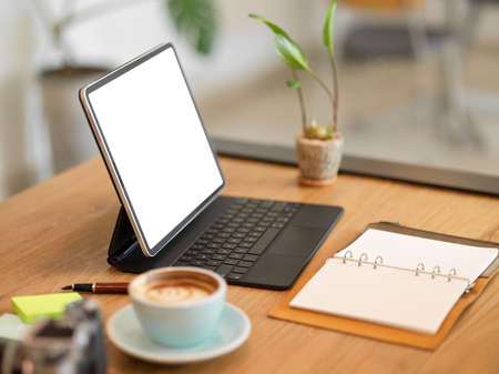 Closeup image of Portable digital tablet with keyboard stand on table at cafe workspace. coffee cup, blank diary on tableの写真素材