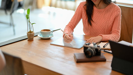 Young female freelance blogger in comfy sweater using stylus pen on tablet computer to create her online content.の写真素材