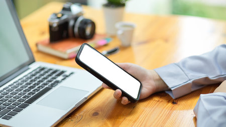 Close-up businesswoman's hand holding smartphone blank screen mockup for montage your application banner. office workspace.の写真素材