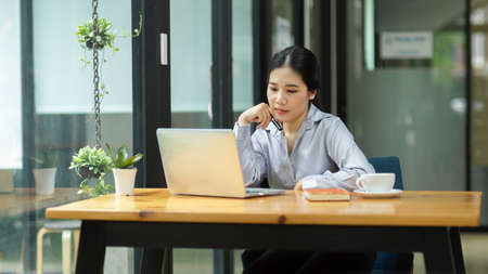 Young female business worker working on her laptop computer, thinking and ponder on her strategy ideasの写真素材