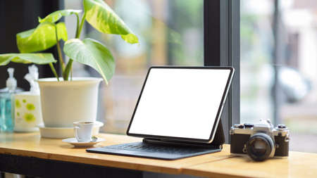 Tablet computer blank screen mockup, vintage retro camera, coffee cup, indoor plant on table over blurred backgroundの写真素材