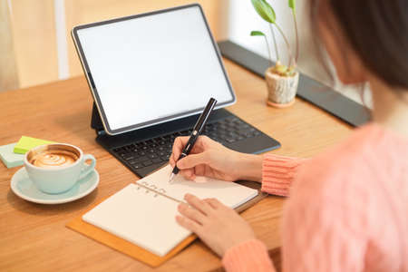 Close-up Asian female business owner, college student, businesswoman working on tablet while writing an information on her book.の写真素材