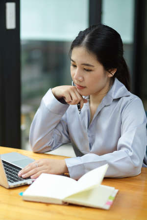 Portrait of Thoughtful asian businesswoman working and analysing business financial statement on laptop computer.の写真素材