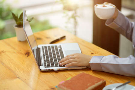 Close-up Successful businesswoman drinking hot coffee during working on laptop computer in the morning at cafe.の写真素材