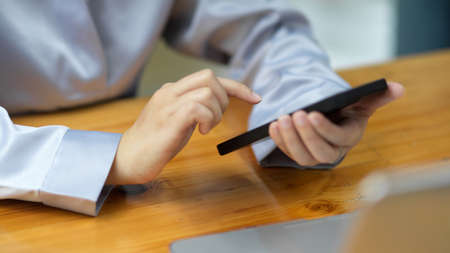 Close-up Female businesswoman using a modern smart phone on her desk to play mobile games, shop online, and relax.の写真素材
