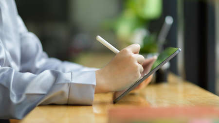 Close-up, side view of businesswoman, female entrepreneur using tablet and stylus pen at her workspace.の写真素材