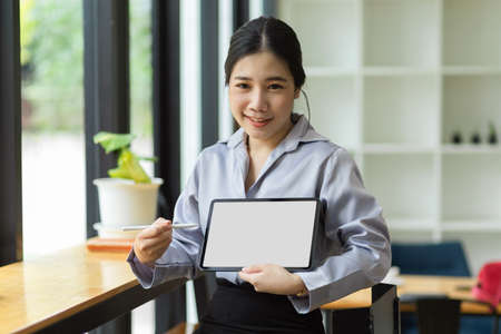 Young asian business worker holding and showing digital tablet computer with blank screen mockup for montage graphic.の写真素材