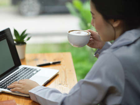 Young businesswoman drinking and sipping coffee while working on her laptop computer and designing her presentation process.の写真素材
