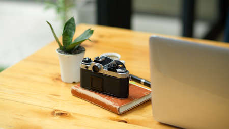 Close-up, back side of vintage camera on diary, laptop computer and plant in a small pot on wooden table.の写真素材
