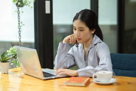 Happy focused asian business woman analysing new strategy and working on her laptop computer in the office.の写真素材
