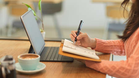 Side view of Female college student studying on her online class and lecturing the importance topics on notebook.の写真素材