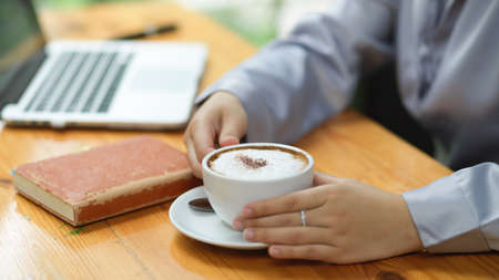 Close-up Businesswoman holding hot cappuccino white coffee cup, drinking coffee during works.の写真素材