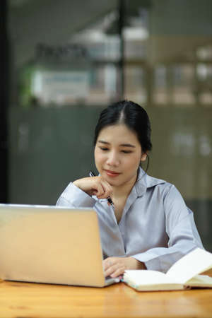 Portrait of Female employee working on her project on laptop computer sits at her desk in the office.の写真素材