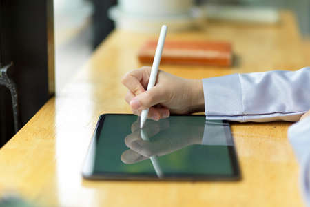 Side view, close-up hand of businesswoman using stylus pen to taking some notes on digital tablet computer on the desk.の写真素材