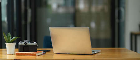 Close-up workspace in the office, laptop computer, camera on a book and decor plant on wooden tableの写真素材