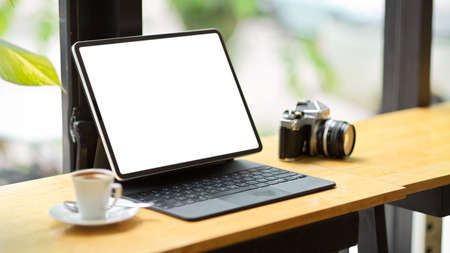 Technology concept, Tablet computer blank screen mockup stand on portable table with retro camera and coffee cup.の写真素材