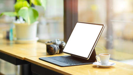 Modern digital tablet computer white screen mockup with keyboard stand on wooden table near large glass window in coffee shop.の写真素材