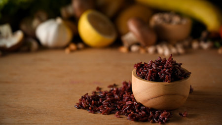 Healthy food concept, Cooked rice berry in a wooden bowl on wooden background with blurred vegetables in background.の写真素材