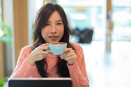 Close-up Pretty young asian female holding coffee cup, drinking morning coffee at cafe. relax, chill, calm, rest, coffee therapy.の写真素材