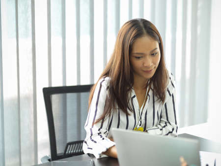 Close-up, Positive businesswomen looking on laptop screen while co working with her team in the meeting room.の写真素材