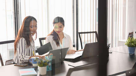 Through the window image of two asian young businesswomen working and planning project together in...