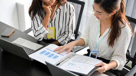 Cropped of two young coworkers working on financial data paperworks while using laptop computer.の写真素材