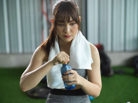 Exhausted fitness woman take some rest and hold vitamin drinking water after weight training at sport centre.の写真素材
