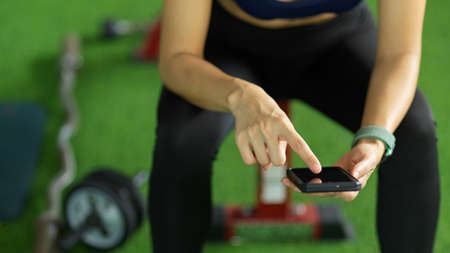 Cropped shot of attractive sporty girl in sportswear using modern smart mobile phone at the gym.の写真素材