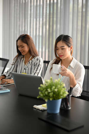 Company's officer working on laptop computer while drinking coffee at her working desk.の写真素材