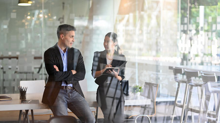 Successful businessman and businesswoman talking the business plan while standing in their workplaceの写真素材