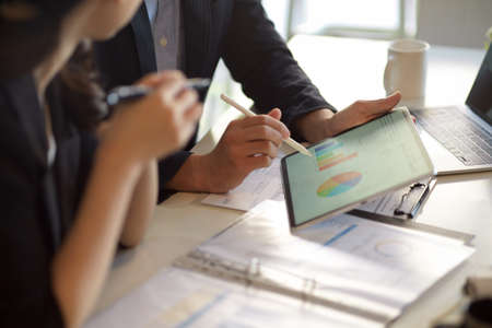 Closeup, businessman showing the business pie chart report via digital tablet computer to businesswoman.の写真素材