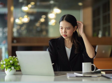 Businesswoman confusing with her financial informations on the report, looking at laptop screen.の写真素材