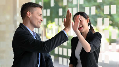 Cheerful businessman and businesswoman giving high five, excited happy, celebrating, goal achievement.の写真素材