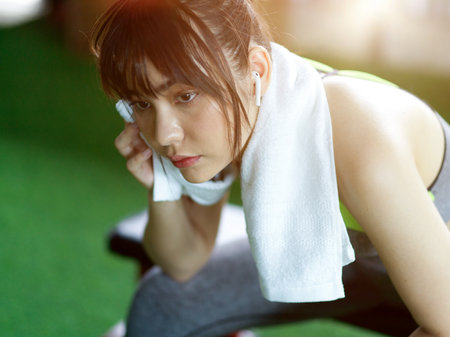Exhausted fitness woman sweating after had a hard body weight training at indoor gym. Female using towel.の写真素材